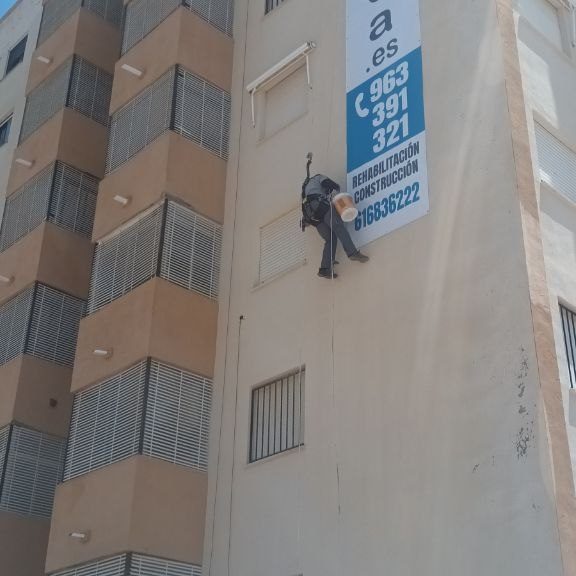 Trabajos verticales Obrero colgado de unos arneses en una fachada con un cubo.