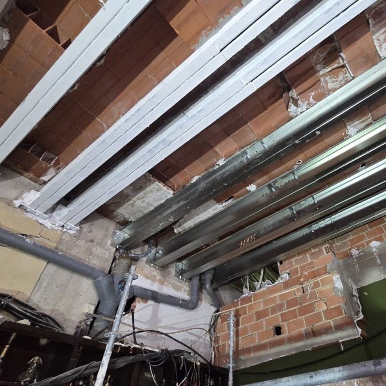 Refuerzo estructural Dos obreros en un sótano reforzado con andamios arreglando una pared
